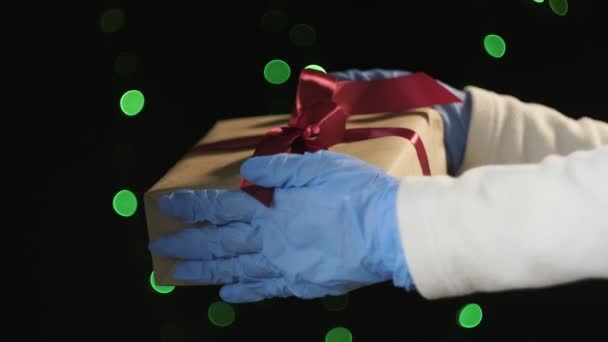 Primer plano en las manos en guantes protectores azules que sostienen la caja de regalo con cinta roja — Vídeos de Stock