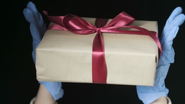 Manos de las personas en guantes protectores azules que sostienen la caja de regalo con cinta roja — Vídeos de Stock