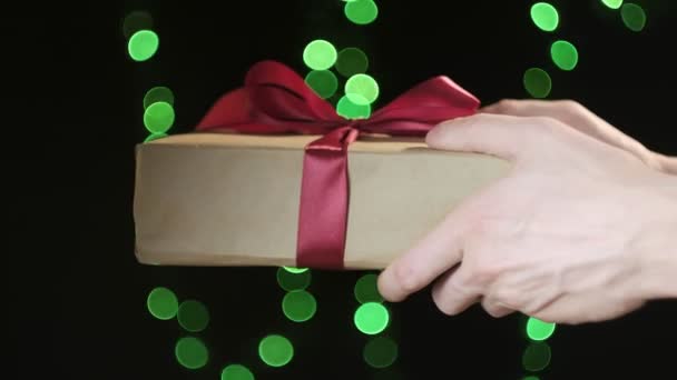 Hands hold christmas gift box with red ribbon on background of green light bokeh — Stock Video