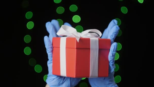 Manos en guantes protectores azules sosteniendo caja de regalo roja con cinta blanca, primer plano — Vídeo de stock