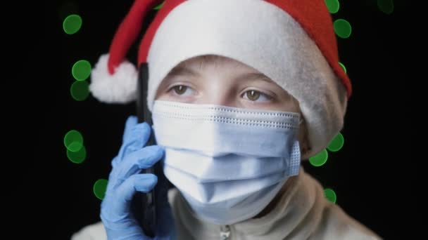 Chica en sombrero de Santa Claus, máscara de protección médica, guantes habla por teléfono móvil — Vídeo de stock