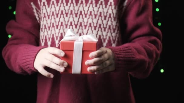 Дитячі руки тримають червону коробку з білою стрічкою. Різдво, концепція нового року — стокове відео