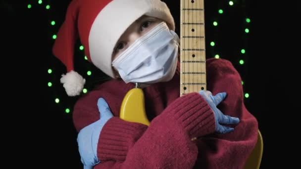 Girl in Santa Claus hat, blue medical protective mask, gloves holds guitar — Stock Video