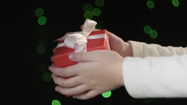 Mains tenant boîte cadeau rouge avec ruban blanc sur fond de lumières vertes bokeh — Video