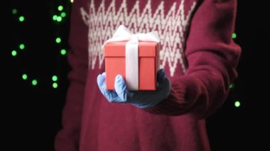 Küçük çocuklar mavi koruyucu eldivenler giyip beyaz kurdeleli hediye kutusu veriyorlar.