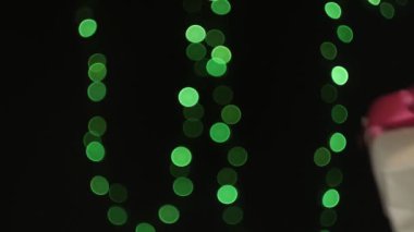 Eller, yeşil ışık Bokeh 'in arka planında kırmızı kurdeleli Noel hediyesi kutusu verir.