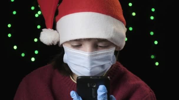 Kırmızı Noel Baba şapkalı kız, mavi koruyucu maske, eldivenler cep telefonuyla konuşuyor. — Stok video