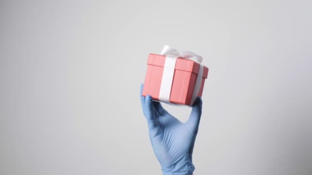 Nahaufnahme in blauem Schutzhandschuh mit roter Geschenkbox und weißer Schleife — Stockvideo