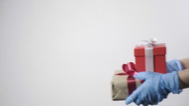 Mavi koruyucu eldivenli birinin elleri hediye kutularına kurdele veriyor. COVID-19 yılbaşı, Noel, doğum günü sürprizi. Karantina güvenliği, yeni normal. Erkekler hediyelerini beyaz arkaplanda verirler