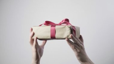 Kırmızı kurdeleli bir adamın eline yakın çekim. Noel, yeni yıl, doğum günü, Sevgililer Günü, uluslararası kadınlar günü sürprizi. Beyaz arkaplandaki kutuda bulunan kişi