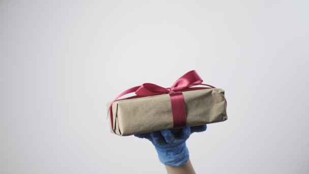 Hand in hand in blauwe beschermende handschoen geeft geschenkdoos met lint. COVID-19 Kerstmis — Stockvideo