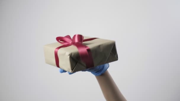Handen i blå skyddshandske ger presentförpackning med band. COVID-19 jul — Stockvideo