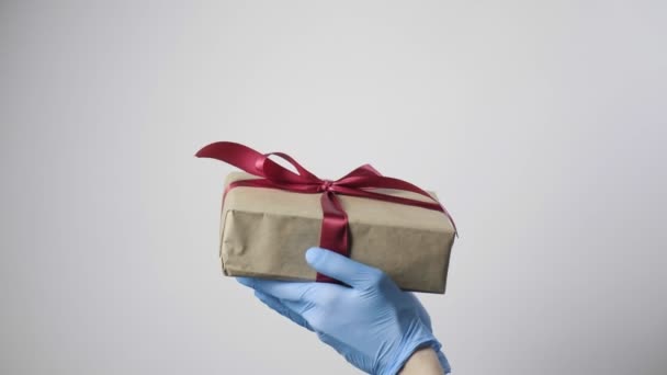 Gros plan sur les mains dans des gants de protection bleus tenant boîte cadeau avec ruban rouge — Video