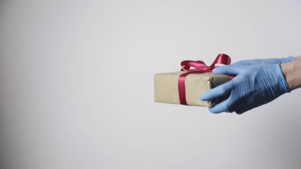 Руки в синіх захисних рукавичках дарують різдвяний подарунок з червоною стрічкою дитині — стокове відео
