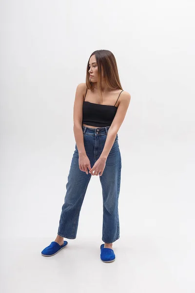 Jeune femme asiatique séduisante aux cheveux longs en haut noir, jeans bleu sur blanc — Photo