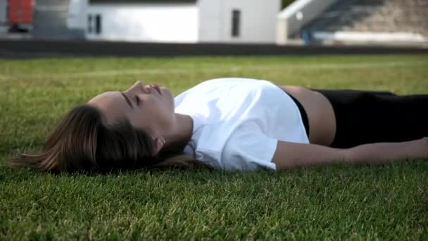 Молодая азиатка в черных леггинсах лежит на зеленой лужайке — стоковое видео