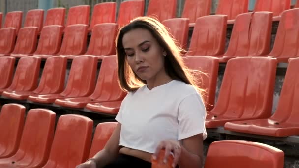 Sportliches hübsches Weibchen sitzt auf der Tribüne, trinkt Wasser aus Plastikflasche — Stockvideo