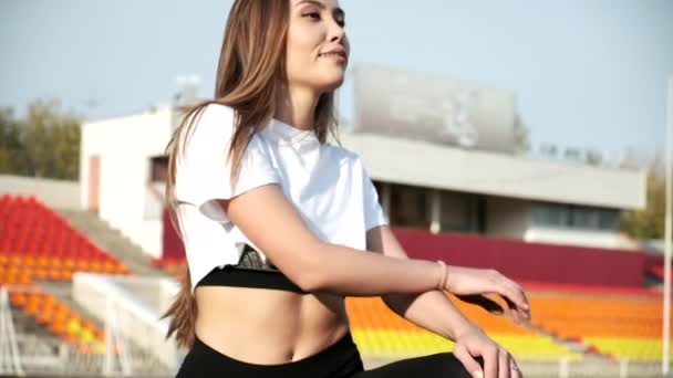 Junge Asiatin in Sportbekleidung streckt an sonnigem Tag die Beine auf dem Stadionplatz — Stockvideo