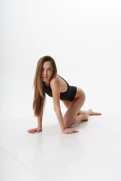 長い髪をしたセクシーなアジア人女性が白いスタジオの背景に黒いランジェリー姿で裸の足でポーズ 膝の上に立つ魅力的な女性 スキニーレディーのボディスーツのモデルテスト — ストック写真