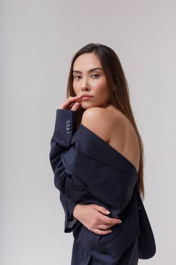 Mavi takım elbiseli genç çekici Asyalı kadın gri stüdyo arka planında izole edilmiş.