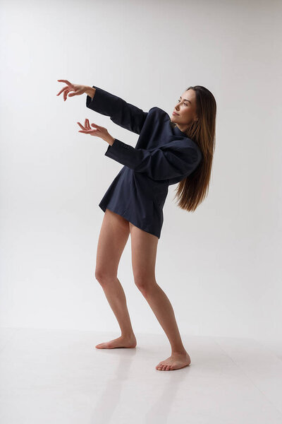 young attractive asian woman in blue suit dancing on white studio background