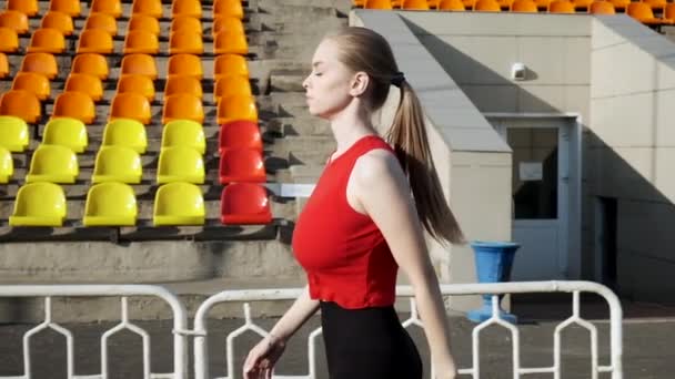 Підходить біла красива жінка в спортивному одязі ходить уздовж трибуни на відкритому повітрі — стокове відео