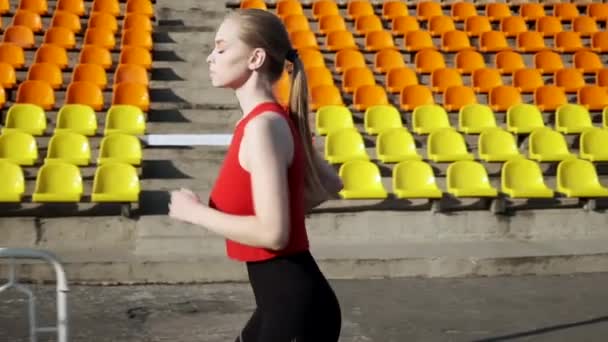 Ταιριάζει καυκάσιος όμορφη γυναίκα στα αθλητικά τρέχει κατά μήκος statium tribune σε εξωτερικούς χώρους — Αρχείο Βίντεο