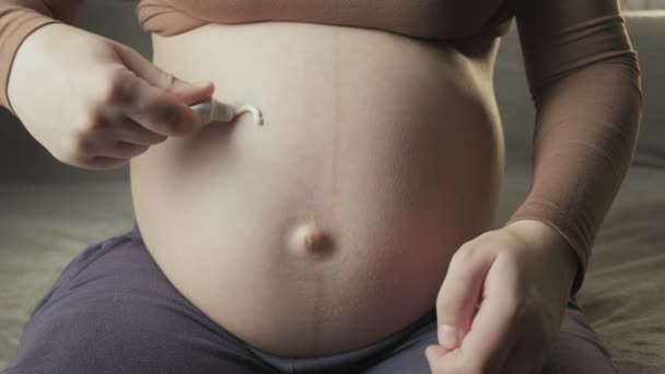 Mujer embarazada dibujando el símbolo del corazón con crema blanca para el cuidado de la piel en su vientre — Vídeo de stock