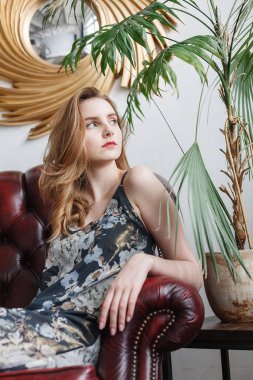 Kafkasyalı, sıska, uzun kahverengi saçlı kadın rahat bir odada koltukta oturuyor.