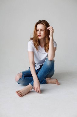 young caucasian woman posing in t-shirt, ripped jeans, sitting on studio floor
