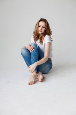 young caucasian woman posing in t-shirt, ripped jeans, sitting on studio floor