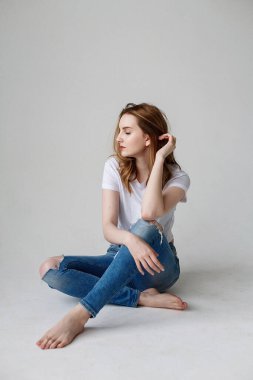 young caucasian woman posing in t-shirt, ripped jeans, sitting on studio floor