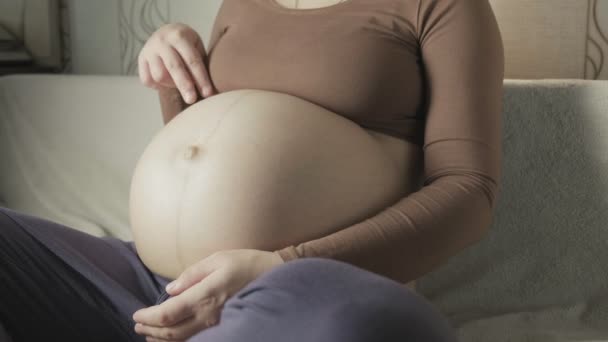 Pregnant woman sitting on couch, playing with belly, stepping on it with fingers — Stock video