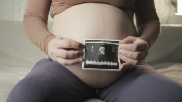 Вагітна животик і жіночі руки тримають зображення сонограми здорової ненародженої дитини — стокове відео
