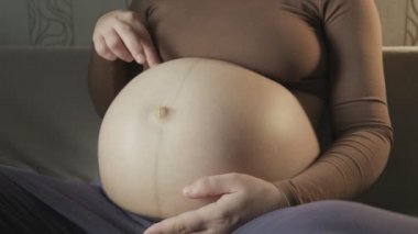 pregnant woman sitting on couch, playing with belly, stepping on it with fingers