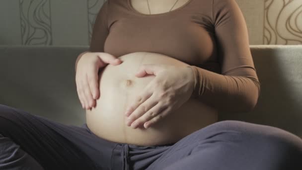 Giovane donna incinta accarezzando grande pancia sul divano, rendendo la forma del cuore con le mani — Video Stock