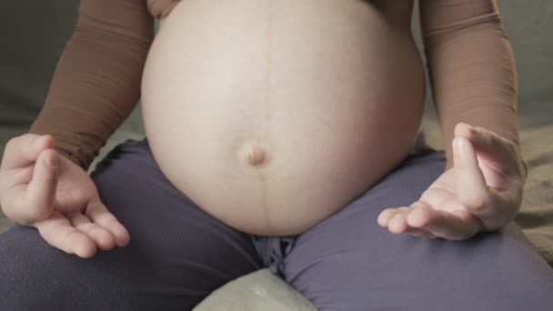 Pregnant lady with large bare tummy meditates sitting in lotus position on sofa — Stock Video