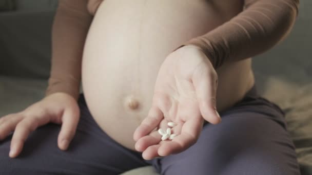 Closeup on pregnant woman with belly sitting on sofa, showing and taking pills — Stock videók