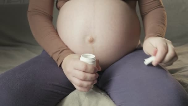 Беременная женщина сидит на диване, открывает бутылку таблеток, показывает лекарства — стоковое видео