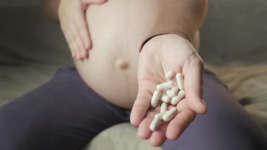 pregnant woman with big belly sitting on couch, showing bunch of pills in palm