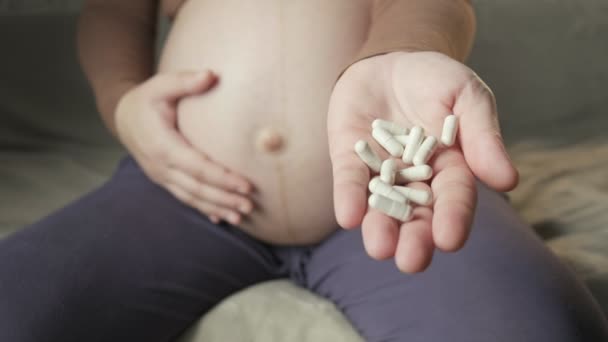 Pregnant woman with big belly sitting on couch, showing bunch of pills in palm — Vídeo de Stock