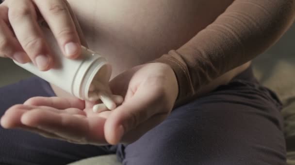 Pregnant woman with big belly sitting on couch, showing bunch of pills in palm — Video Stock