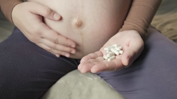 Pregnant woman sitting on couch, holding bunch of pills in palm, stroking belly — Vídeos de Stock