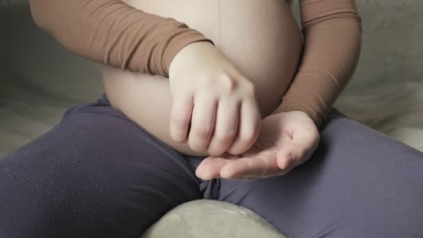 Pregnant woman sitting on couch, pouring out fish oil from bottle on her palm — Stock video