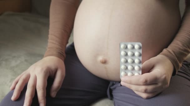 Pregnant woman sitting on couch, holding package of pills in palm, strokes belly — Stok video