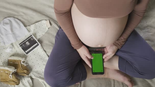 Attesa donna incinta con grande pancia utilizzando smartphone con cromakey sul letto — Video Stock