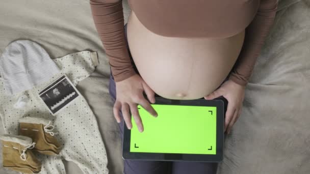 Expecting pregnant woman with large belly using tablet with chromakey on bed — Stock Video