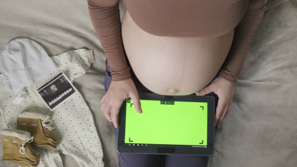 Spodziewa się kobiety w ciąży z dużym brzuchem za pomocą tabletki z chromakey na łóżku — Wideo stockowe