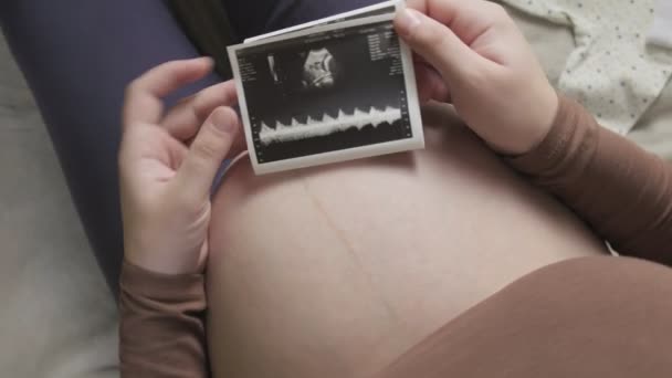 Forventer gravid kvinde med stor mave ser på ultralydsscanning derhjemme – Stock-video