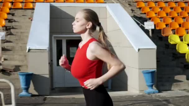 Ταιριάζει καυκάσιος όμορφη γυναίκα στα αθλητικά τρέχει κατά μήκος statium tribune σε εξωτερικούς χώρους — Αρχείο Βίντεο